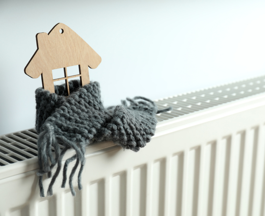 Concept of heating season with wooden house on heating radiator.